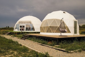 Two dome-shaped structures with transparent sections, a wooden deck, and a hanging chair. - Nomad Space (Bar-Bulak)