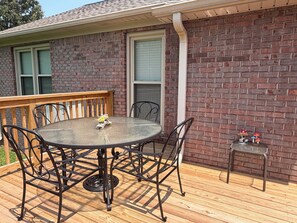 A covered patio with a round table and chairs, a wooden deck, and a brick wall. - Magnolia House In the Cove. Sweet Southern hospitality awaits you here. (Owens Cross Roads)