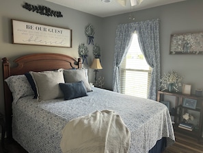 Une chambre à coucher avec une tête de lit en bois, un lit avec plusieurs oreillers, une fenêtre avec des rideaux et un panneau décoratif fixé au mur.