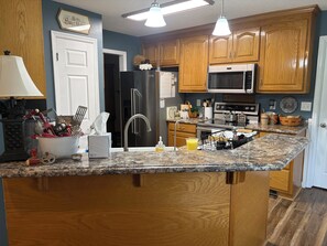 A kitchen with wooden cabinets, a stainless steel refrigerator, a microwave, and a granite countertop. - Magnolia House In the Cove. Sweet Southern hospitality awaits you here. (Owens Cross Roads)