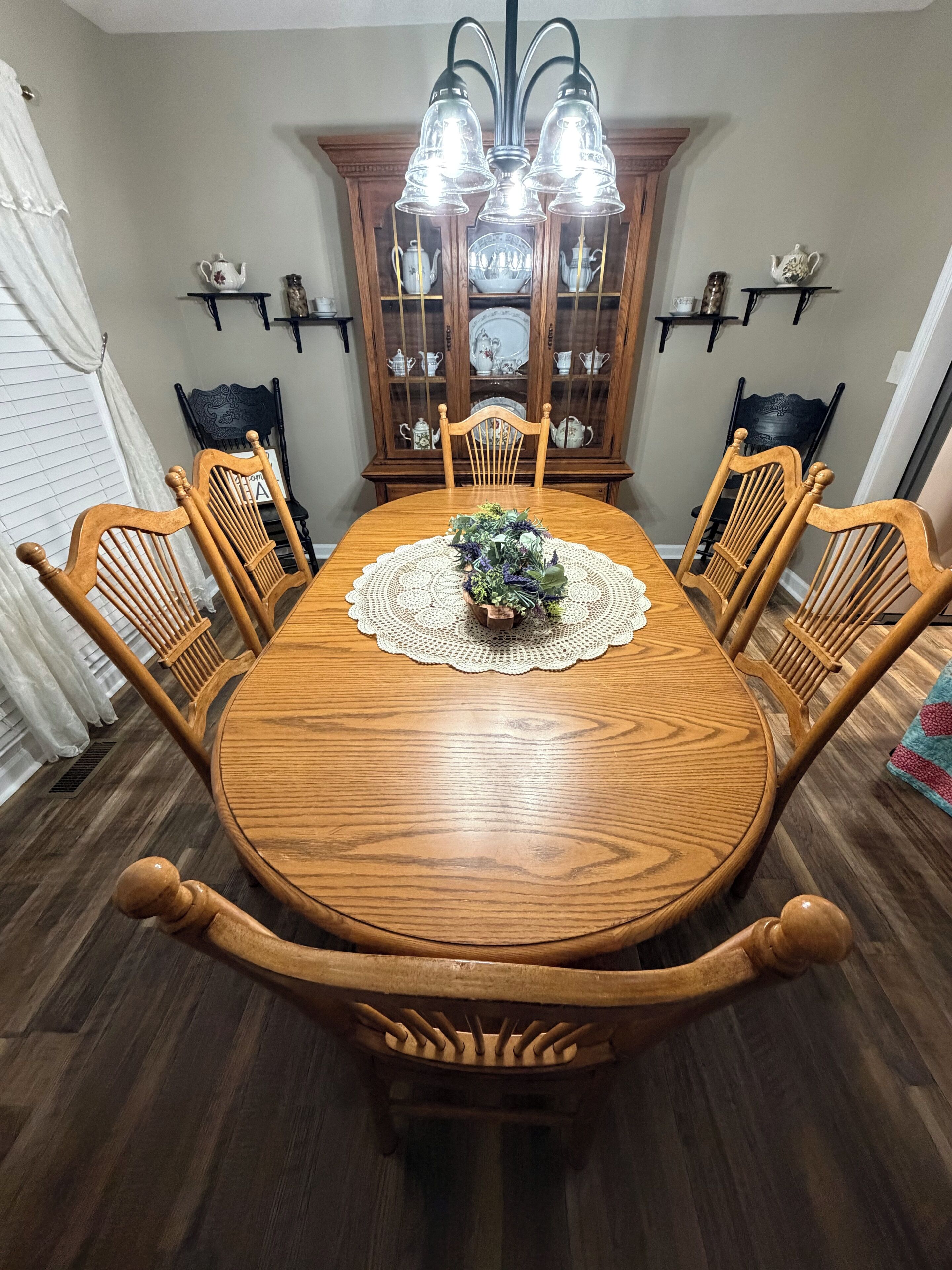 Une salle à manger avec une table en bois, des chaises, un lustre et un buffet.