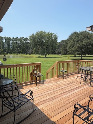 A wooden deck with outdoor furniture, a view of a grassy area with trees, and a clear sky.