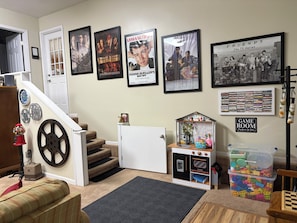 Une pièce avec un escalier, une salle de jeux, une affiche de série télévisée et un panneau indiquant « salle de jeux ».