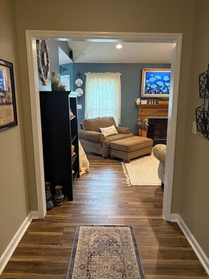 A hallway leading to a living room with a sofa, ottoman, and fireplace.