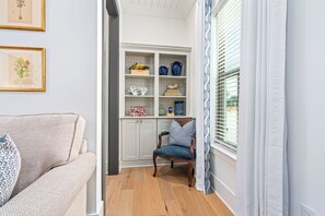 Una sala de estar con un sofá, una silla, una estantería y una ventana con cortinas.