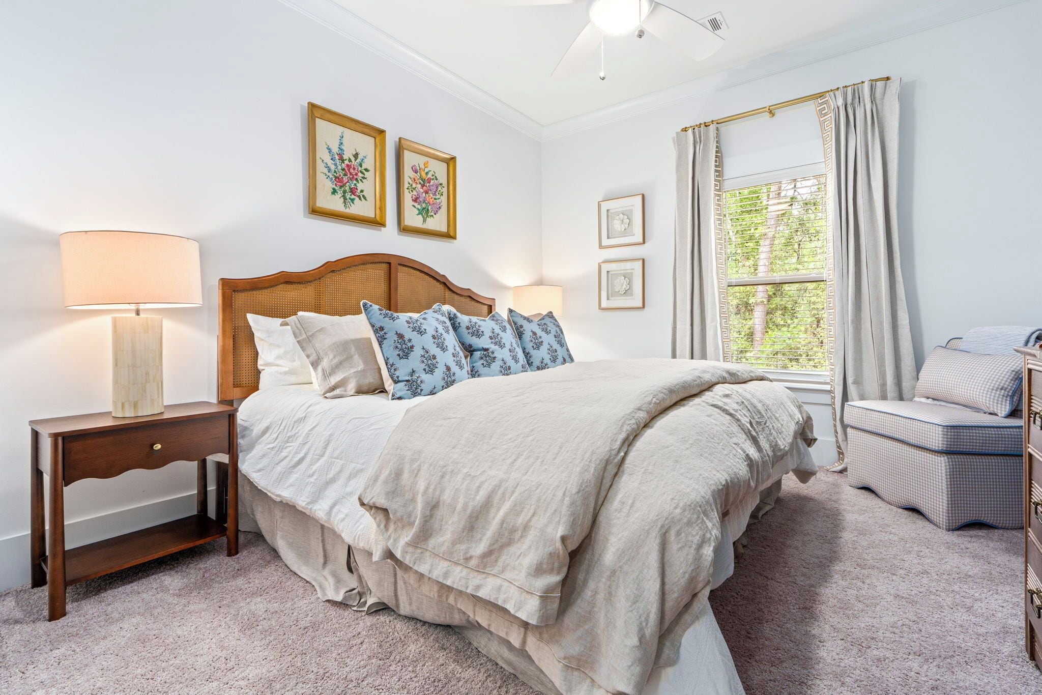 A bedroom with a bed, bedside tables, a lamp, a window with curtains, and framed pictures on the wall.