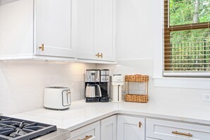 Una cocina moderna con armarios blancos, estufa a gas, cafetera y tostadora.