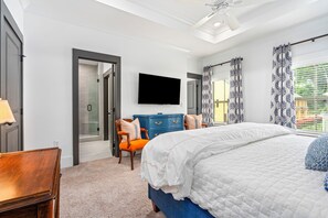 Un dormitorio con cama, cómoda, silla, televisor y puerta que da a un baño.