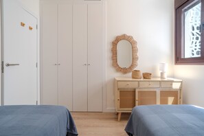 Una camera da letto con due letti, un armadio, un comodino con una lampada, uno specchio e una finestra.