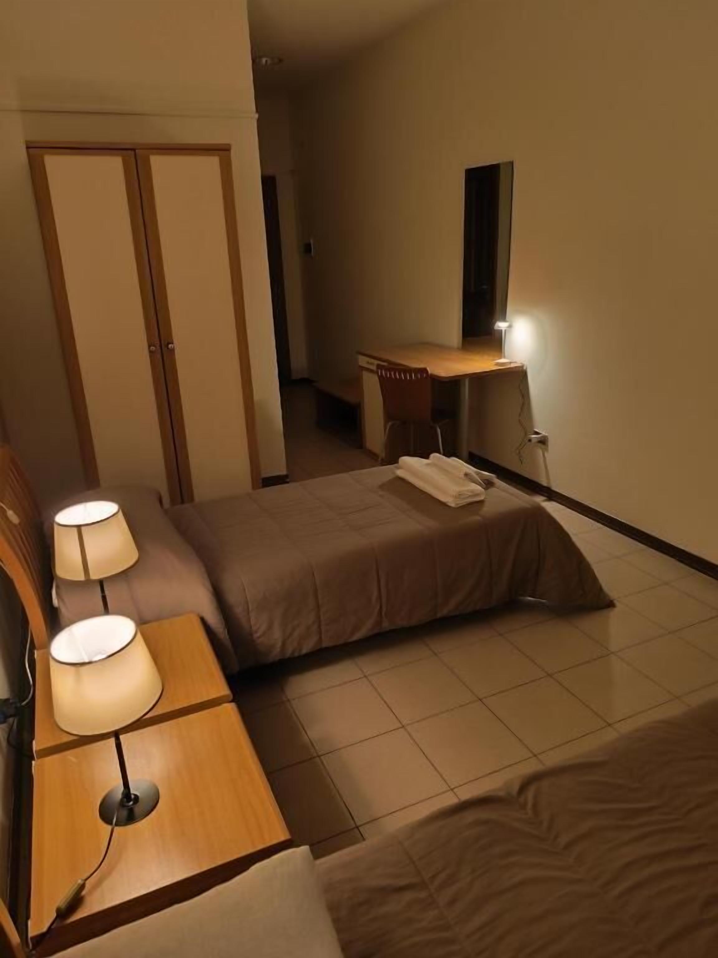 Habitació d'hotel amb un llit, taules de nit amb làmpades, un escriptori amb cadira i un armari.