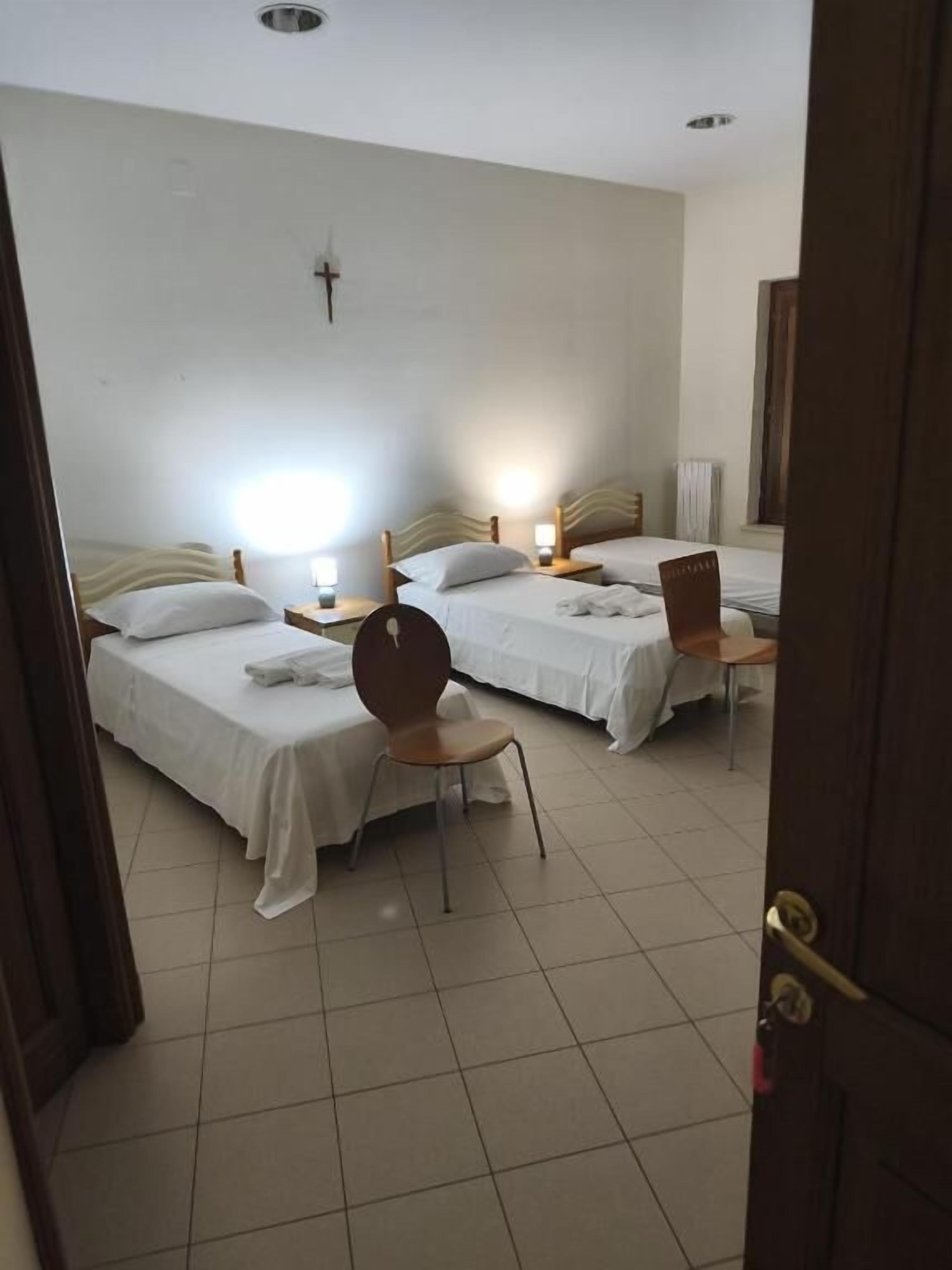 Une chambre d’hôtel avec deux lits, une chaise, une table de chevet et un luminaire fixé au mur.