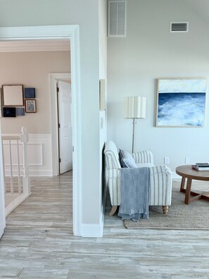 A room with a wooden floor, a white door, a striped sofa, a lamp, and a painting on the wall. - A Rare Bird:Spacious 5-bedroom, beachfront home in welcoming Gulf Shores with AC (Gulf Shores)
