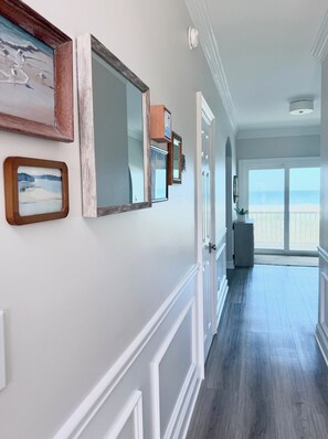 A hallway with framed artwork, a door leading to a balcony, and a view of the beach. - A Rare Bird:Spacious 5-bedroom, beachfront home in welcoming Gulf Shores with AC (Gulf Shores)
