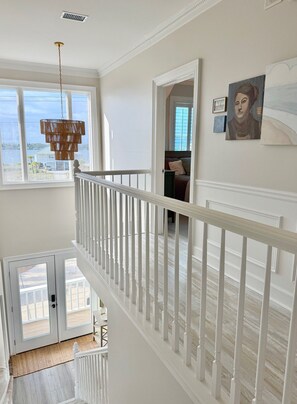 A high-ceilinged room with a white railing, a hanging light fixture, and a view of the outdoors. - A Rare Bird:Spacious 5-bedroom, beachfront home in welcoming Gulf Shores with AC (Gulf Shores)
