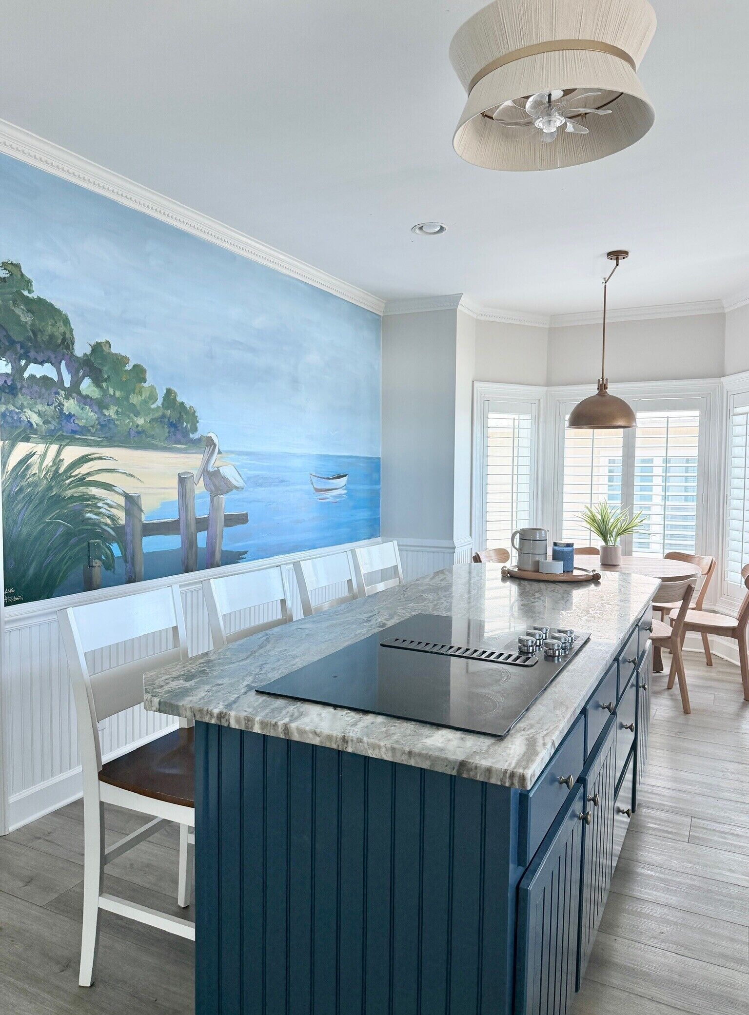 A kitchen with a large island, a painting of a beach scene, and a view of the ocean through the windows.