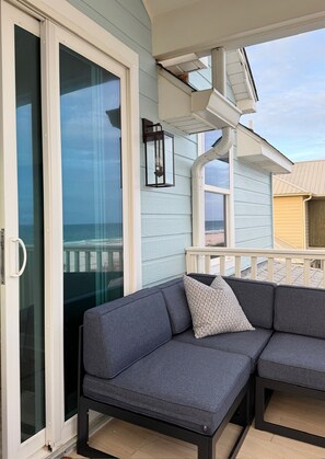 A covered patio area with a gray sectional sofa and a glass door leading to a balcony. - A Rare Bird:Spacious 5-bedroom, beachfront home in welcoming Gulf Shores with AC (Gulf Shores)