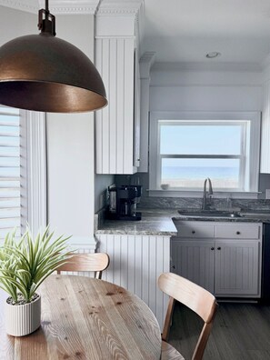 A modern kitchen with a view of the sea, white cabinetry, a wooden dining table, and a pendant light. - A Rare Bird:Spacious 5-bedroom, beachfront home in welcoming Gulf Shores with AC (Gulf Shores)