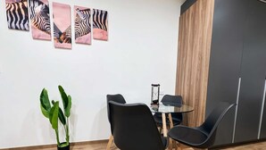 Un espai d'oficina modern amb una taula rodona de vidre, cadires negres, una planta en test i obra d'art amb motius de zebra a la paret.