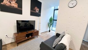 Un saló modern amb televisió plana, un sofà gris, una catifes amb dibuixos i obres d'art a les parets.