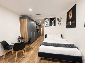 Une chambre moderne avec un lit, une table à manger et des chaises, un coin cuisine et des œuvres d’art accrochées aux murs.