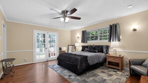 A bedroom with a bed, a ceiling fan, a window with curtains, a nightstand, a chair, and a small table. - Peaceful Dallas Retreat Near Downtown & Fair Park (Dallas)