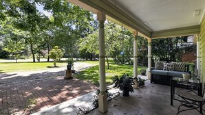 A covered porch with a brick pathway leading to a grassy area, a seating area with a sofa, and potted plants. - Peaceful Dallas Retreat Near Downtown & Fair Park (Dallas)