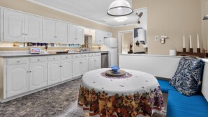 A kitchen with white cabinets, a dining table with a floral tablecloth, and a blue sofa with a patterned pillow. - Peaceful Dallas Retreat Near Downtown & Fair Park (Dallas)