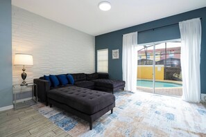 Una sala de estar con un sofá modular, una lámpara y vista a una piscina a través de un ventanal.