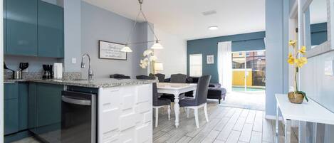 A modern kitchen with a built-in dishwasher, a dining area with a white table and chairs, and a view of a swimming pool.