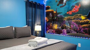Ein Hotelzimmer mit Bett, Nachttisch, Lampe und Wandgemälde mit Unterwasser-Szene.