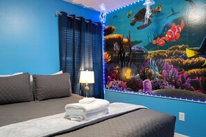 Ein Hotelzimmer mit Bett, Nachttisch, Lampe und Wandgemälde mit Unterwasser-Szene.