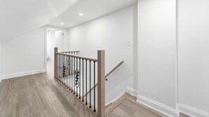 Een verzorgde, moderne hal met een houten vloer, witte muren en een houten trap voorzien van een metalen leuning.
