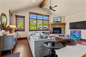 A living room with a fireplace, large windows, a ceiling fan, and a television. - Perfect Family Getaway: 3BR with Hot Tub and Stunning Alpine Views (Keystone)