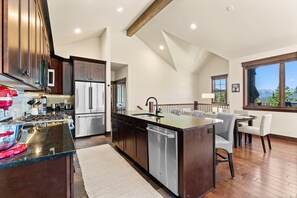 A modern kitchen with stainless steel appliances, a central island, and a dining area with a view. - Perfect Family Getaway: 3BR with Hot Tub and Stunning Alpine Views (Keystone)