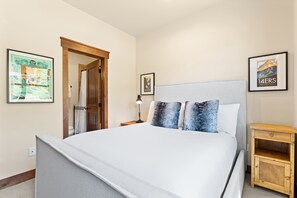 A hotel room with a large bed, a wooden nightstand, a small wooden cabinet, and two framed pictures on the wall. - Perfect Family Getaway: 3BR with Hot Tub and Stunning Alpine Views (Keystone)