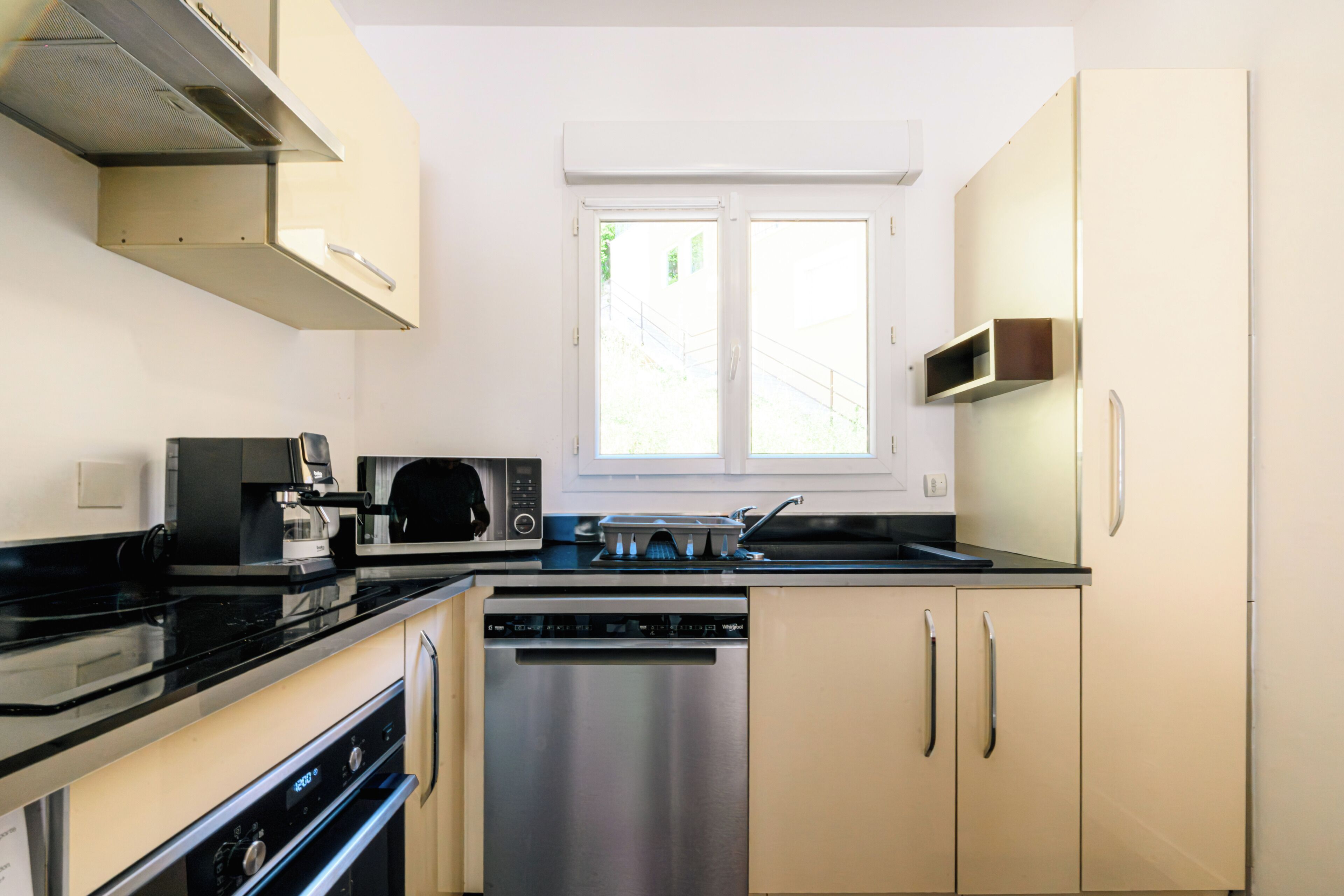 A modern kitchen with a dishwasher, oven, microwave, and a window above the sink.