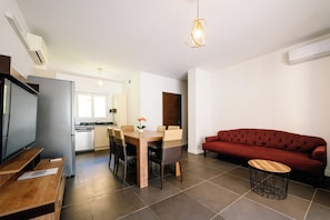 A modern living space with a dining area, a red sofa, a TV, and a kitchen in the background. - Quartz 5 Apartment (Cannes)