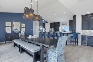 A modern kitchen with dark cabinets, a marble countertop, and a dining area with a bench and chairs. - Oceanfront with heated pool and hot tub (North Topsail Beach)
