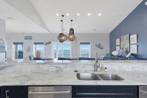 A modern kitchen with a marble countertop, stainless steel sink, and pendant lights. - Oceanfront with heated pool and hot tub (North Topsail Beach)