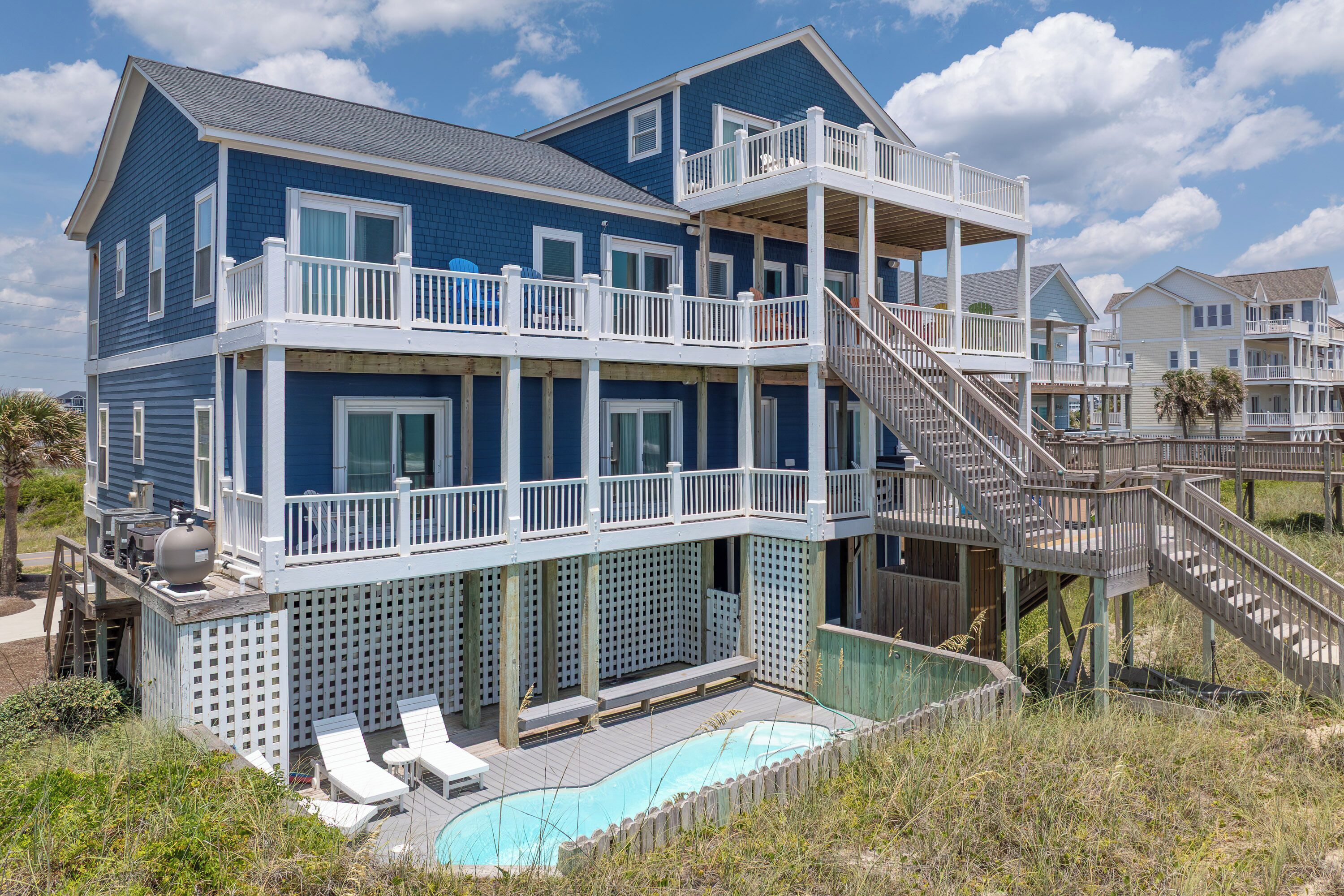 A two-story beachfront house with a balcony, a pool, and a staircase leading to the upper level.