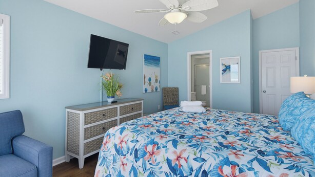A bedroom with a bed, a TV, a ceiling fan, and a door. - Oceanfront with heated pool and hot tub (North Topsail Beach)