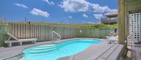 Una terraza de madera con piscina, sillas de descanso y un cerco de madera.