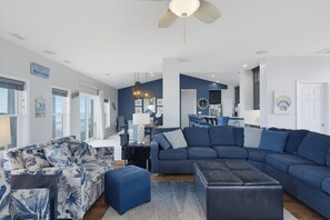 A spacious living area with a sectional sofa, ottomans, and a dining area with chairs. - Oceanfront with heated pool and hot tub (North Topsail Beach)