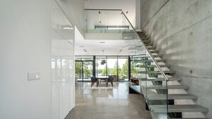 A modern interior with a glass staircase, a dining area, and large windows. - Modern Luxury Lakehouse (Stone Mills)