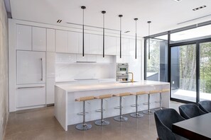 Een moderne keuken met een centraal eiland, barkrukken en een groot raam met uitzicht op bomen.
