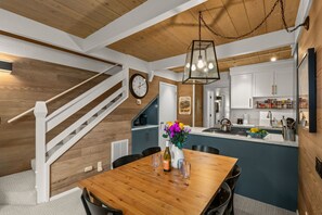 Una cocina moderna con armarios blancos, una isla de madera y una zona de comedor con mesa y sillas de madera.