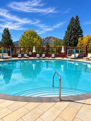 A swimming pool with lounge chairs and umbrellas, surrounded by trees and mountains. - Sun Valley Dollar Meadows Retreat - access to Sun Valley Inn pool/hot tub/tennis (Sun Valley)
