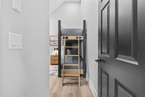 Un couloir étroit avec un lit superposé, une échelle en bois, une table de chevet avec une lampe et une porte.
