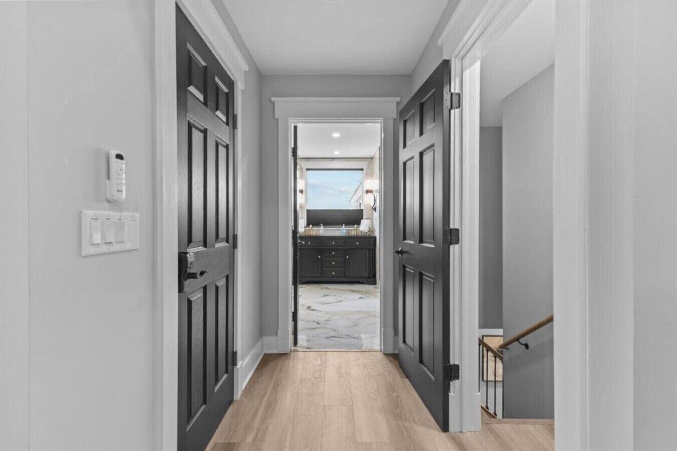 A hallway with dark wooden doors, a light switch, and a marble floor leading to a kitchen area.