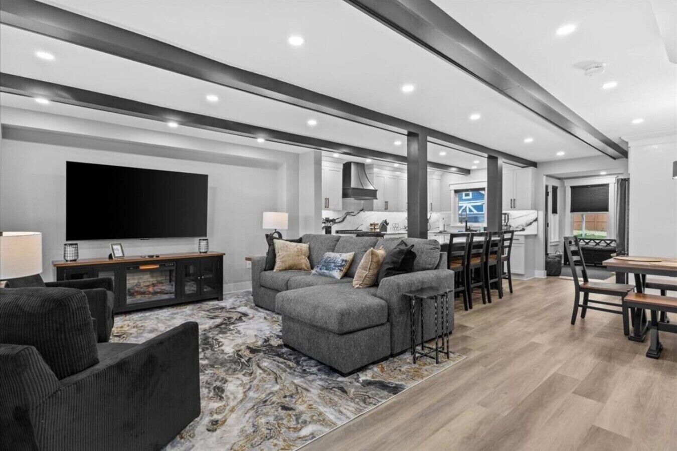 A modern living room with a grey sofa, a flat-screen TV, and a dining area with a wooden table and chairs.
